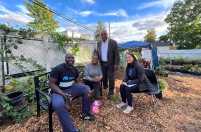 3 people sitting on benches and smiling with one person standing and smiling next to one of the benches.